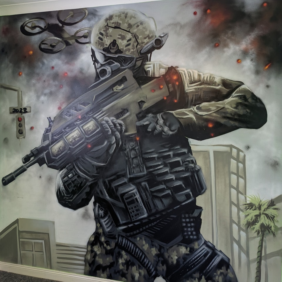 Grayscale spray-painted mural depicts a call of duty futuristic soldier in full tactical gear holding a weapon, surrounded by smoke, explosions, and a surveillance drone in an urban setting.
