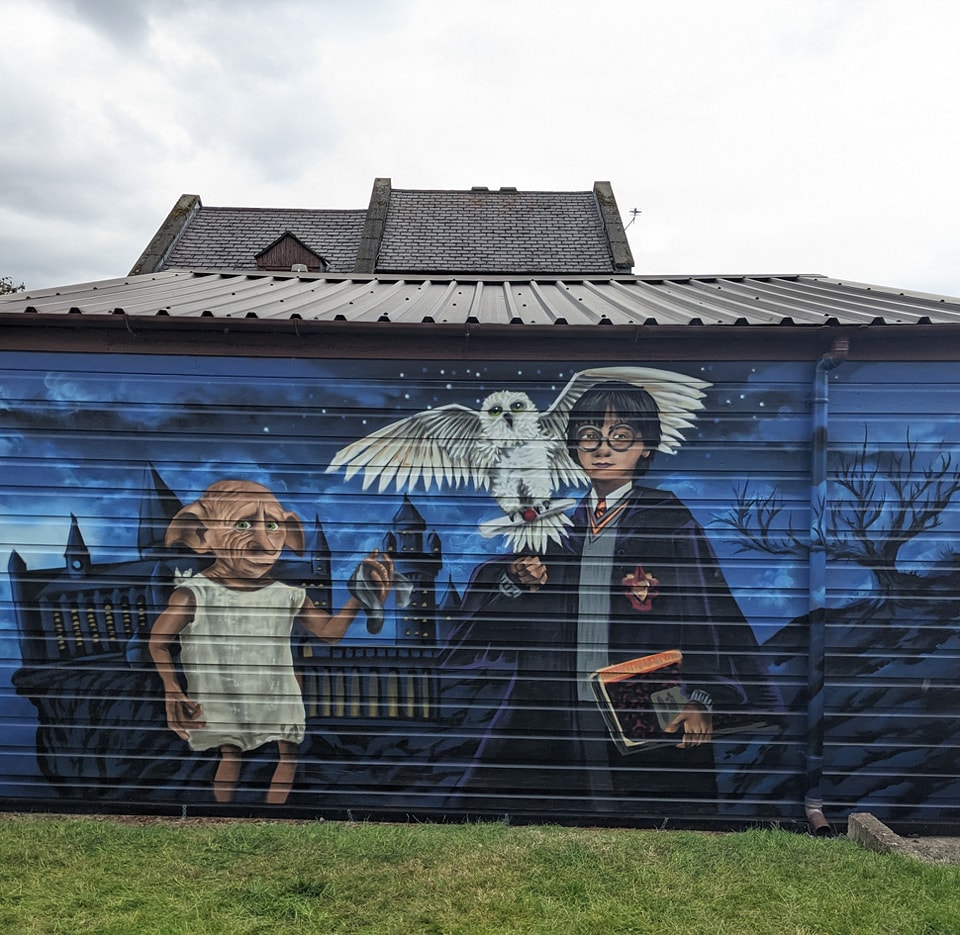 Mural on a garage door featuring Harry Potter, Hedwig, and Dobby in front of Hogwarts under a starry night sky.