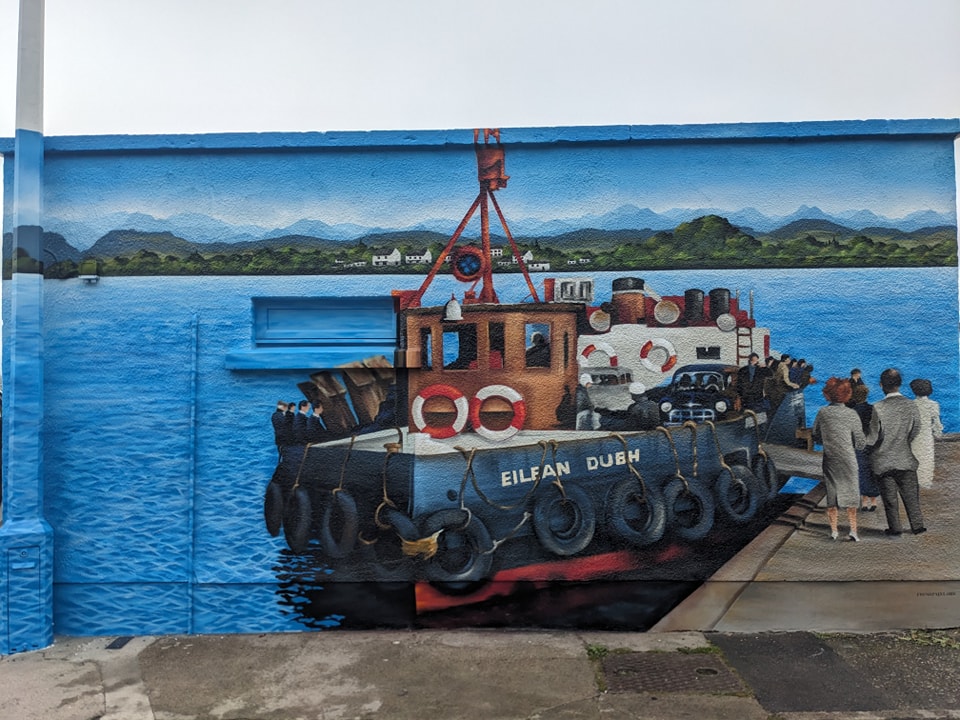 Mural depicting the ferry boat Eilean Dubh docked on bright blue water with a crowd of people waiting on the North Kessock pier against a backdrop of green hills.